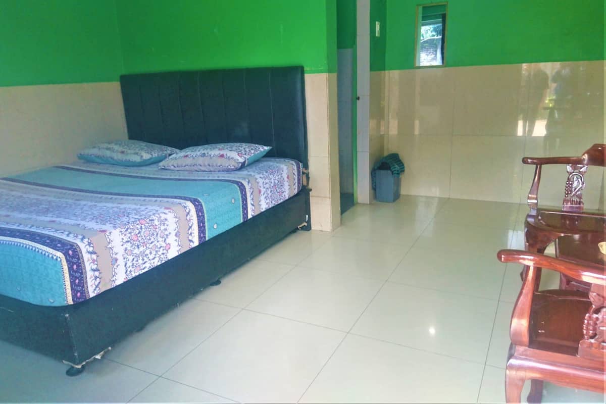 A room with a bed, a chair, and a trash bin.