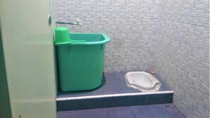 A small, enclosed bathroom with a toilet, a green trash bin, and a white sink. - Hotel Bukit Panembahan (Durin Simbelang)