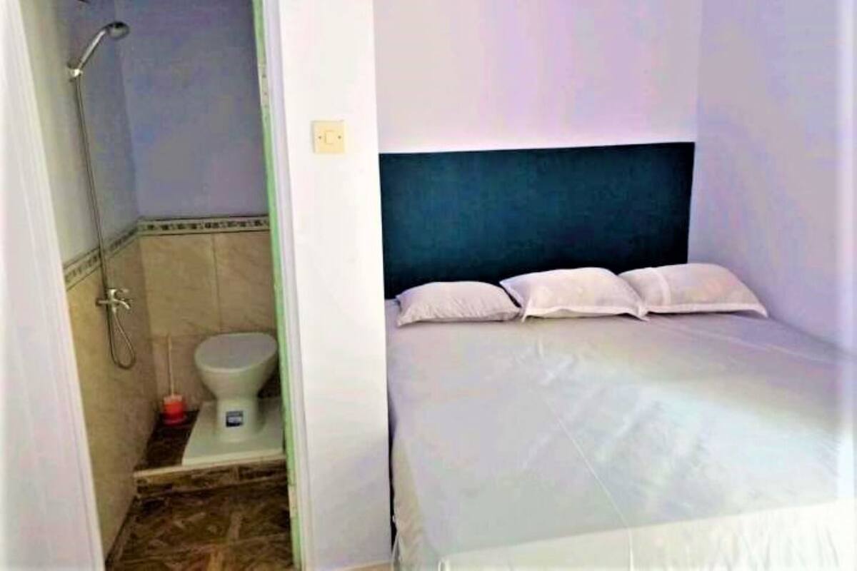 A small, single-room hotel room with a bed, a toilet, and a shower.