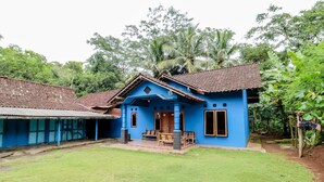 Una casa azul con techo de tejas, un porche con muebles de madera y un césped bien cuidado.