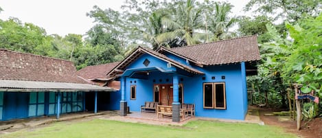 A blue house with a tiled roof, a porch with wooden furniture, and a well-maintained lawn.