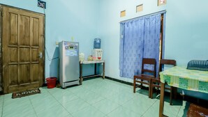 Una habitación pequeña con puerta de madera, un refrigerador, dispensador de agua, una mesa con mantel y una silla.