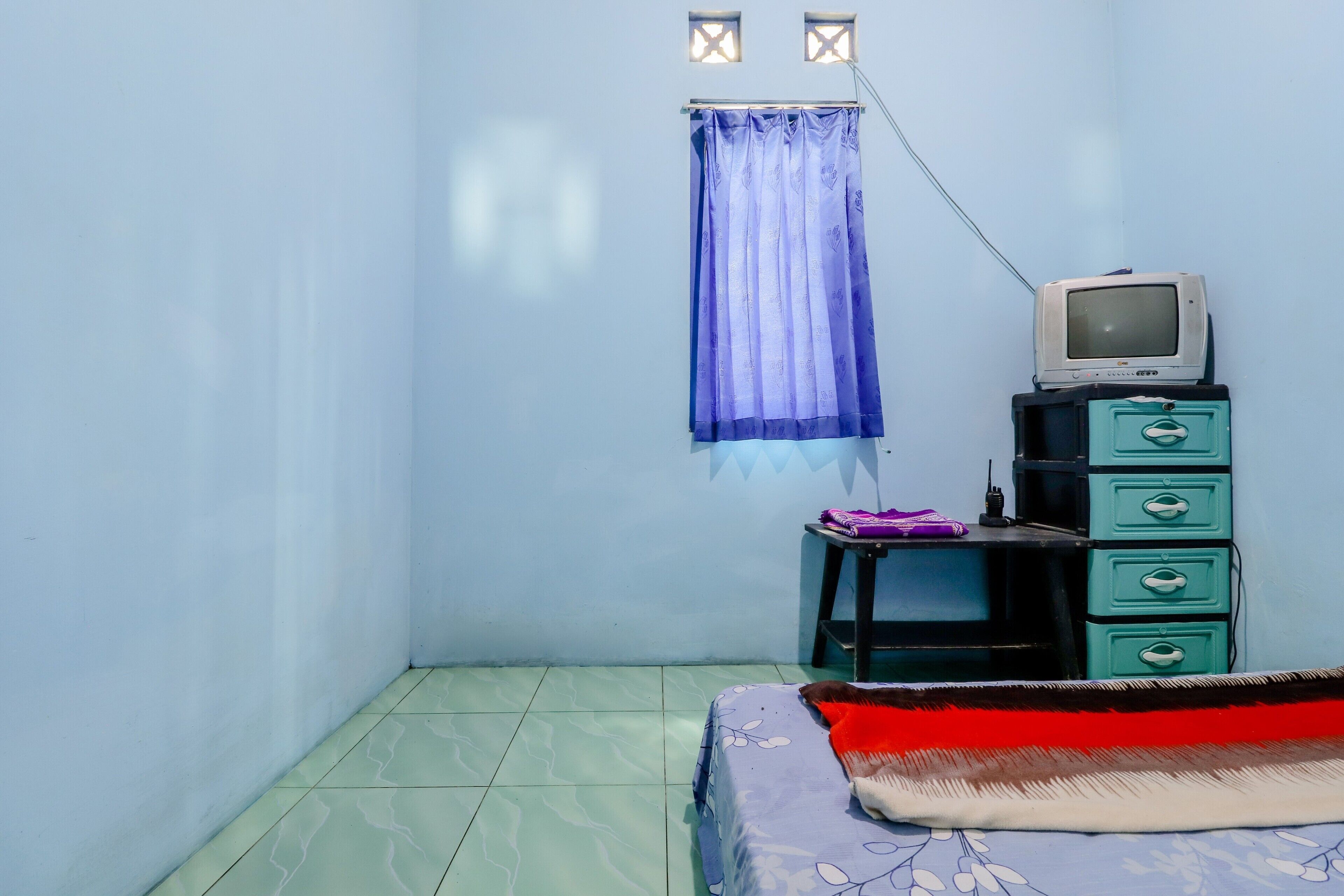 A small room with a bed, a dresser, a television, and a window with a curtain.
