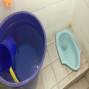 A blue trash bin and a light blue toilet in a bathroom with tiled walls. - Penginapan Tasya (Kalirejo)