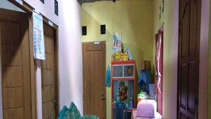 A narrow hallway with a green sofa, a small table with a pink tablecloth, and a blue chair. - Penginapan Tasya (Kalirejo)