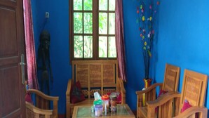 A room with a blue wall, a wooden table with various items, and two wooden chairs. - Penginapan Tasya (Kalirejo)