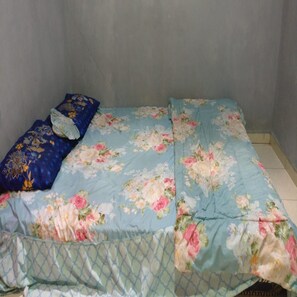 A bed with floral bedding and a blue pillow. - Penginapan Tasya (Kalirejo)