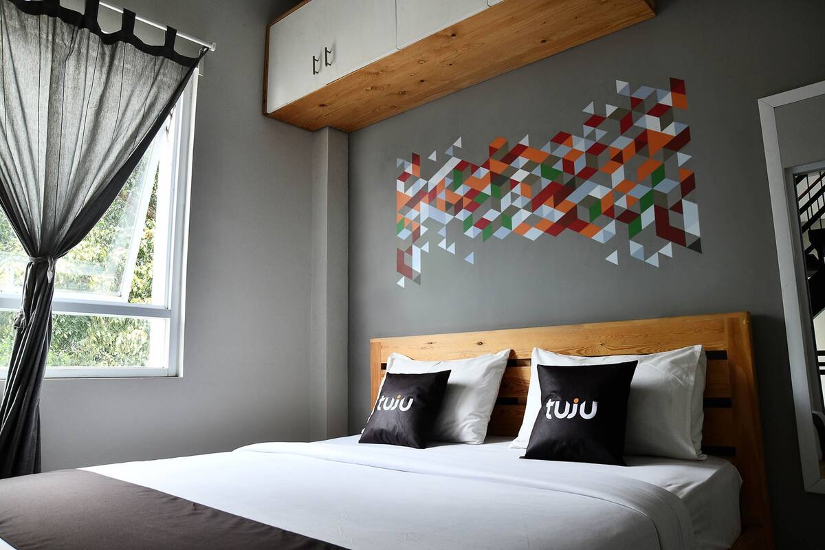 A bedroom with a bed, a geometric wall art, and a window with curtains.
