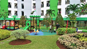 A playground with a slide, swings, and a climbing net, surrounded by well-maintained bushes and trees. - Apartment Green Lake View Ciputat by Celebrity Room (South Tangerang)