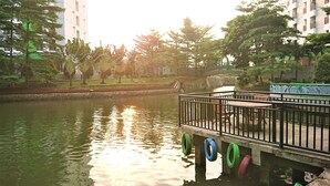 A riverside walkway with a bridge supported by tires, surrounded by greenery and residential buildings. - Apartment Green Lake View Ciputat by Celebrity Room (South Tangerang)