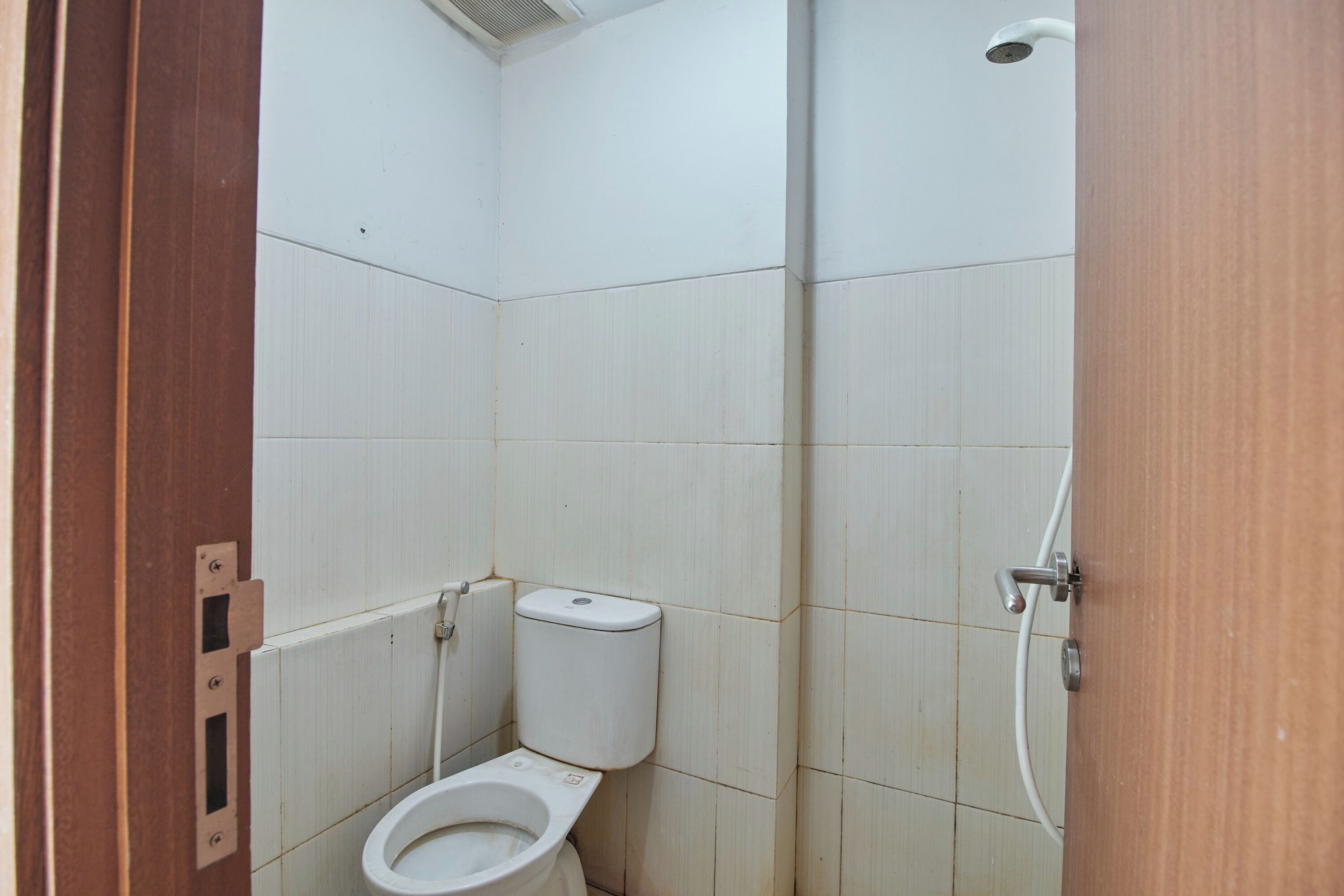 Een kleine, afgesloten badkamer met toilet, douche en een deur.
