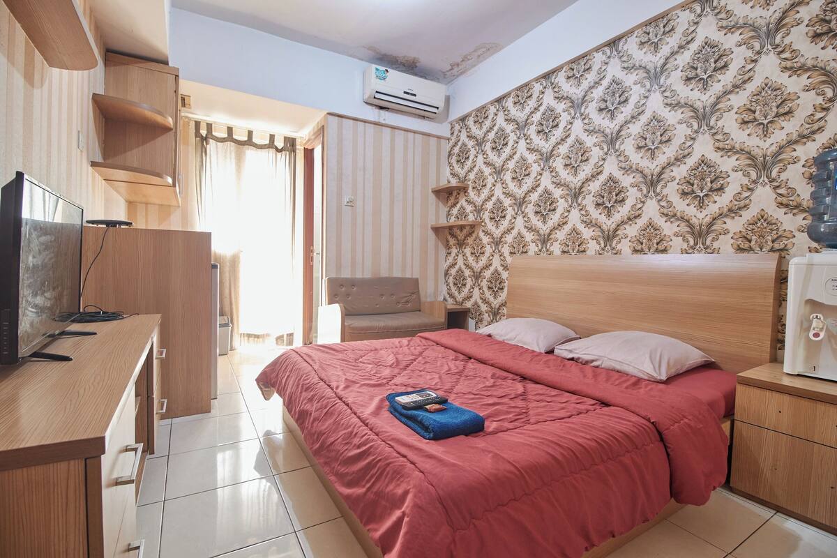 A hotel room with a bed, a desk, a chair, a TV, and an air conditioning unit.