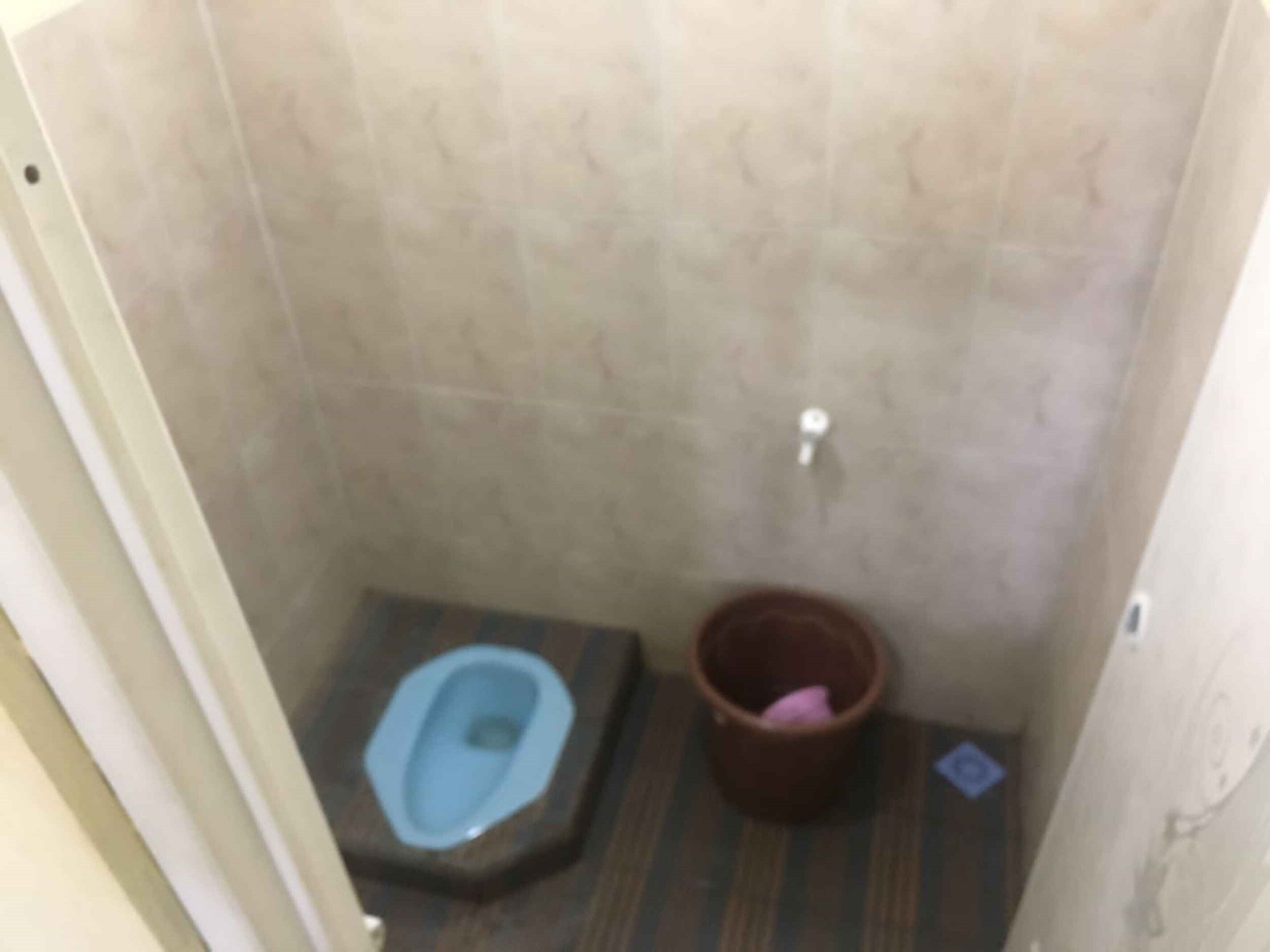 Casa de banho pequena com sanita, um balde e um candeeiro fixado na parede.