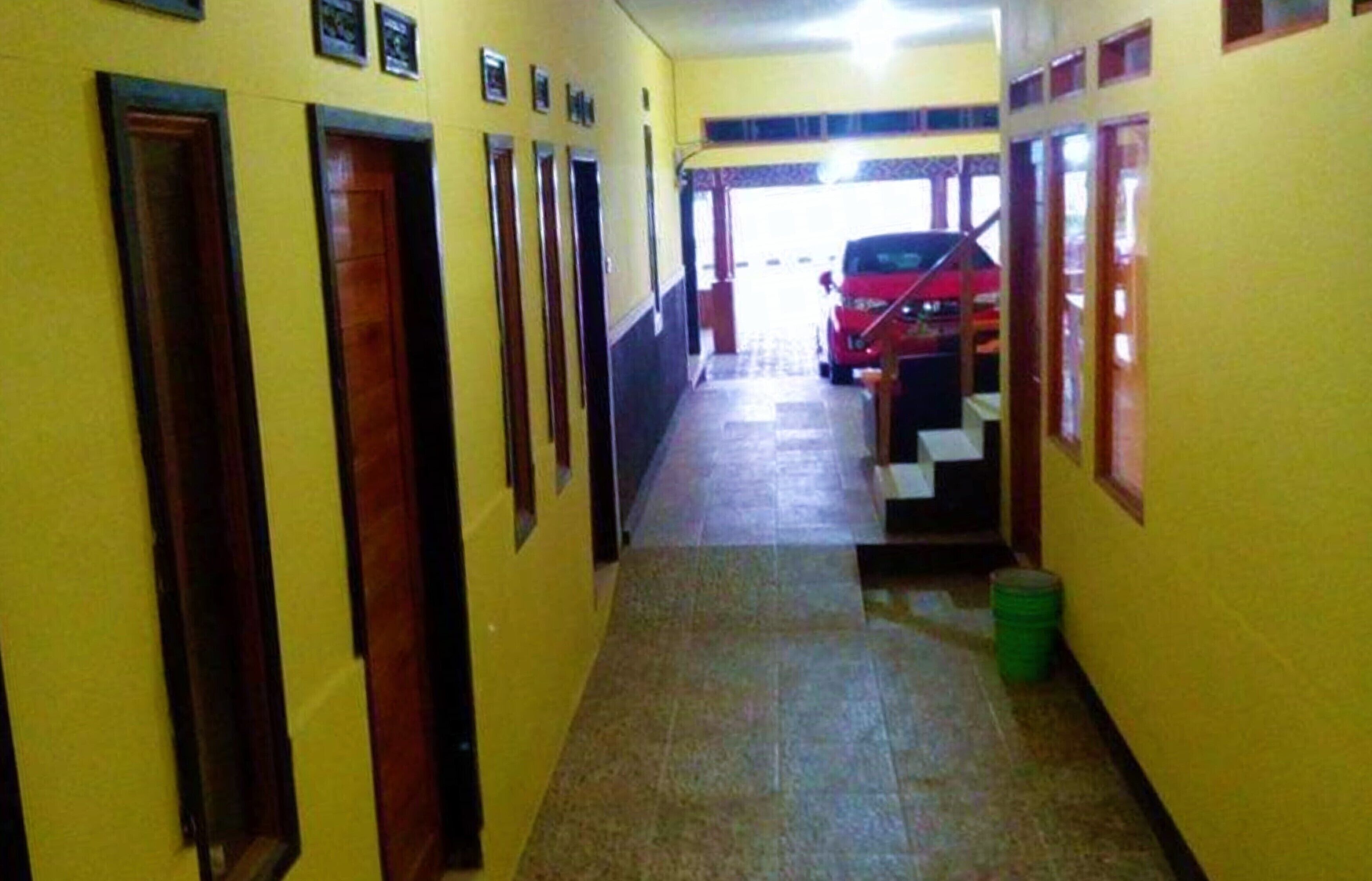 A narrow hallway with doors on one side and a staircase leading to a car parked outside.