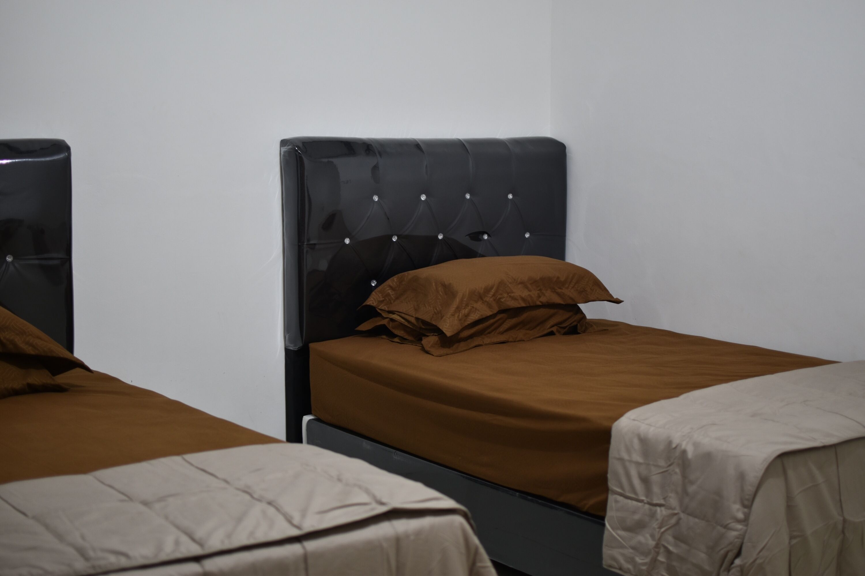 A room with two beds, each with a headboard and a brown bedspread.