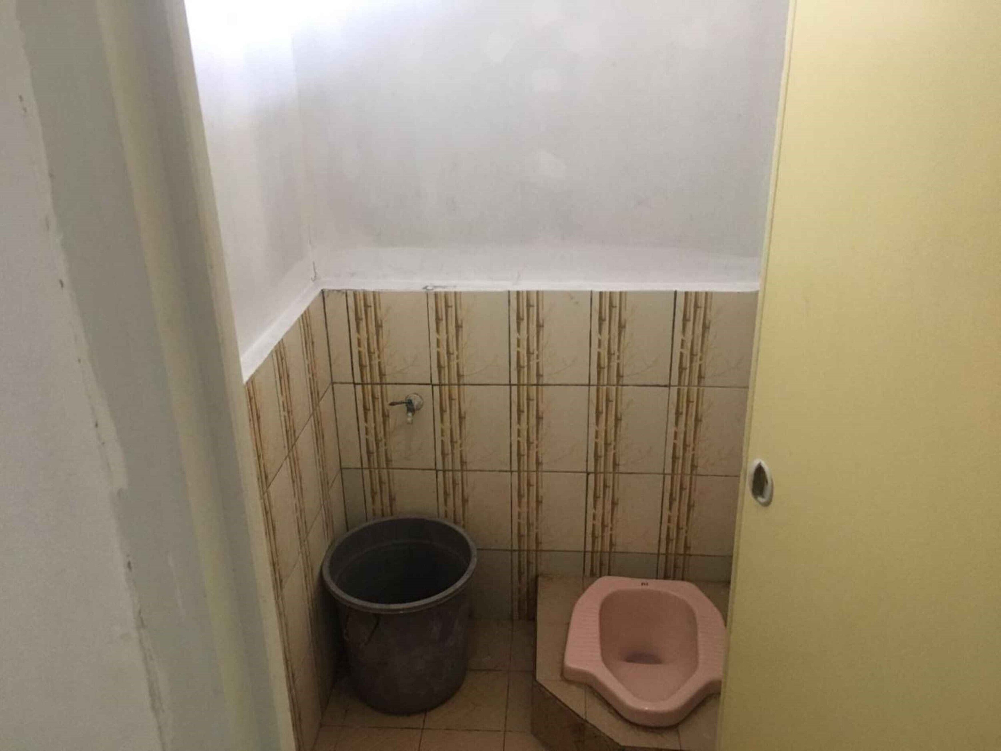 A small bathroom with a toilet, a bucket, and tiled walls.