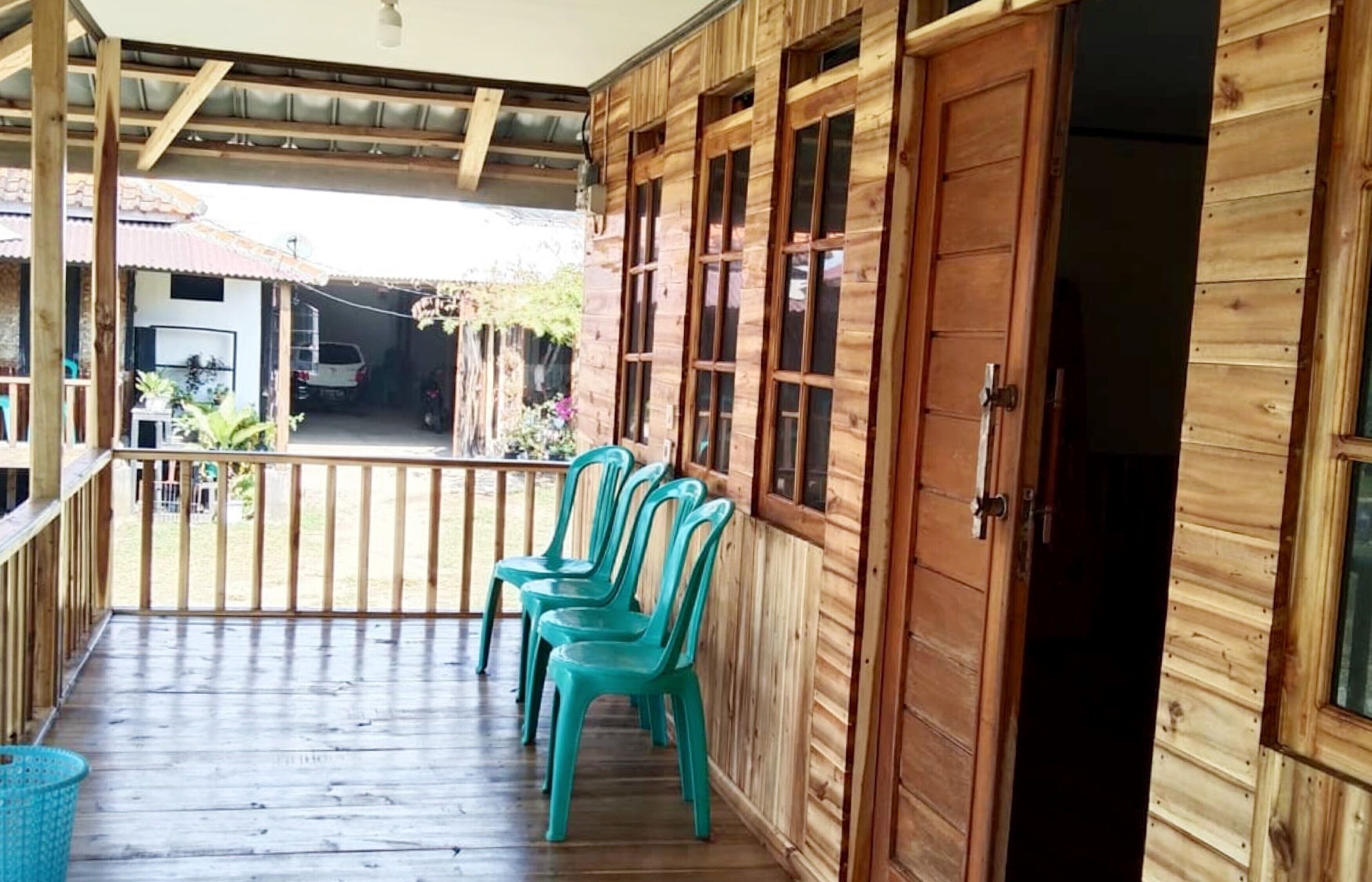 Eine Holzhütte mit Veranda, einer Schiebetür und Blick auf ein Fahrzeug und Grün im Hintergrund.