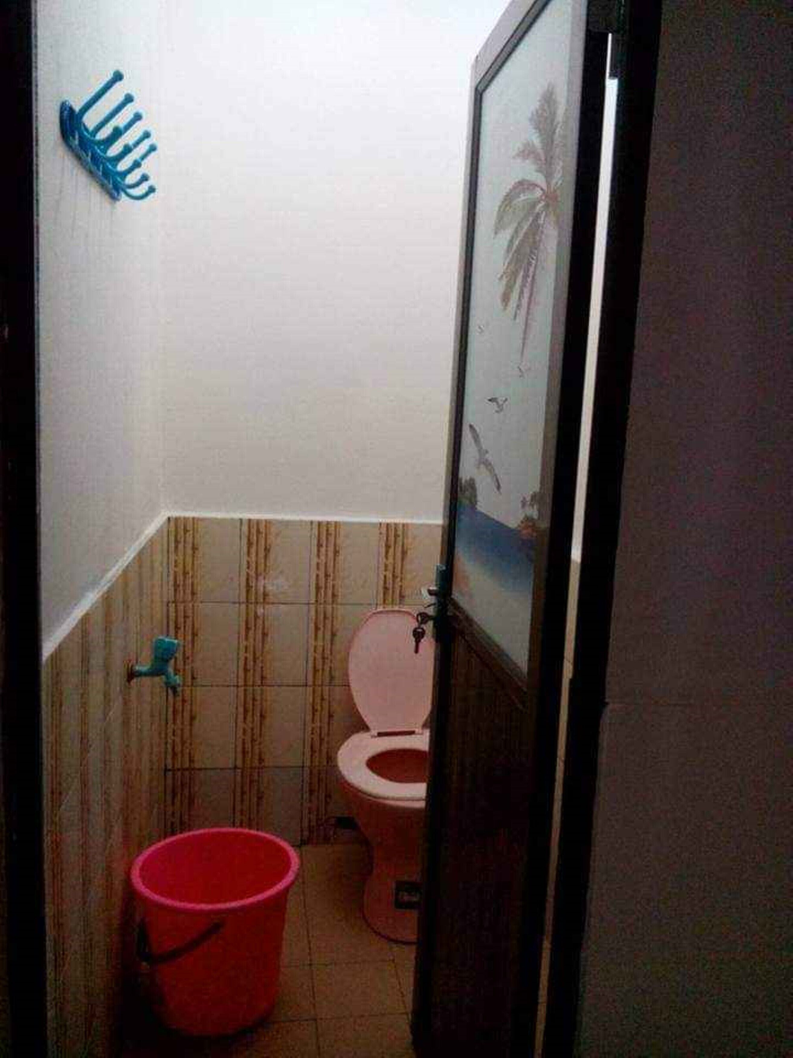 A small bathroom with a toilet, a red bucket, and a blue hook on the wall.