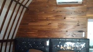 Une chambre avec un plafond en pente, des murs en bois, un lit avec une tête de lit et un appareil de climatisation.