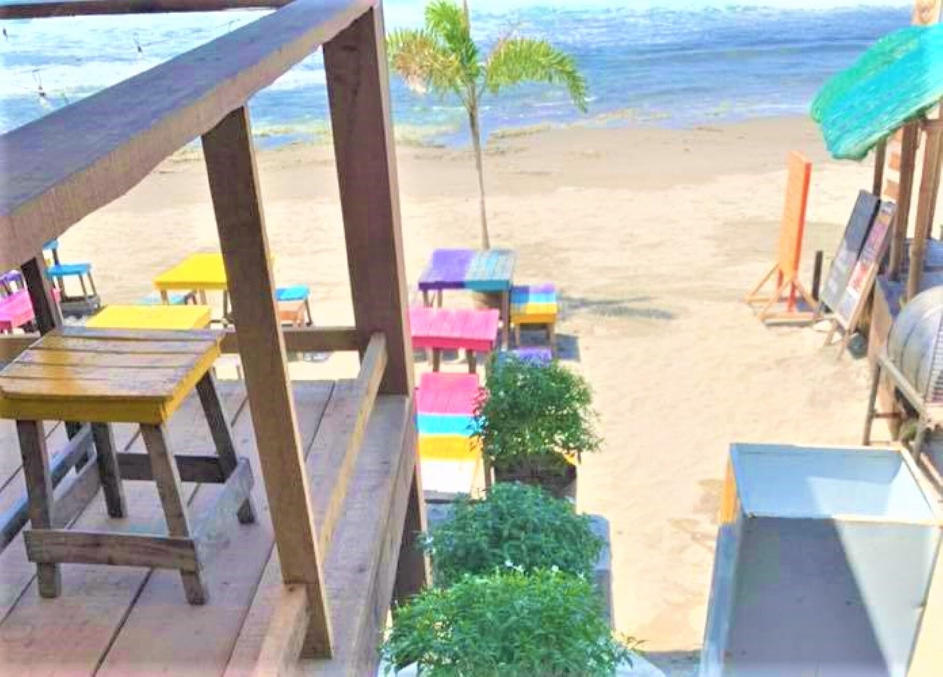 Zona de playa con asientos en terraza de madera, sombrillas coloridas y vistas al océano.