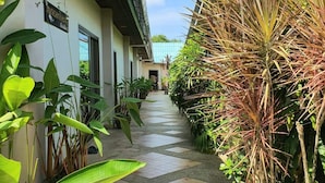 A narrow pathway flanked by lush greenery and a building with a sign reading "BUCHSITTA HOUSE." - Muchshima House (Choeng Thale)