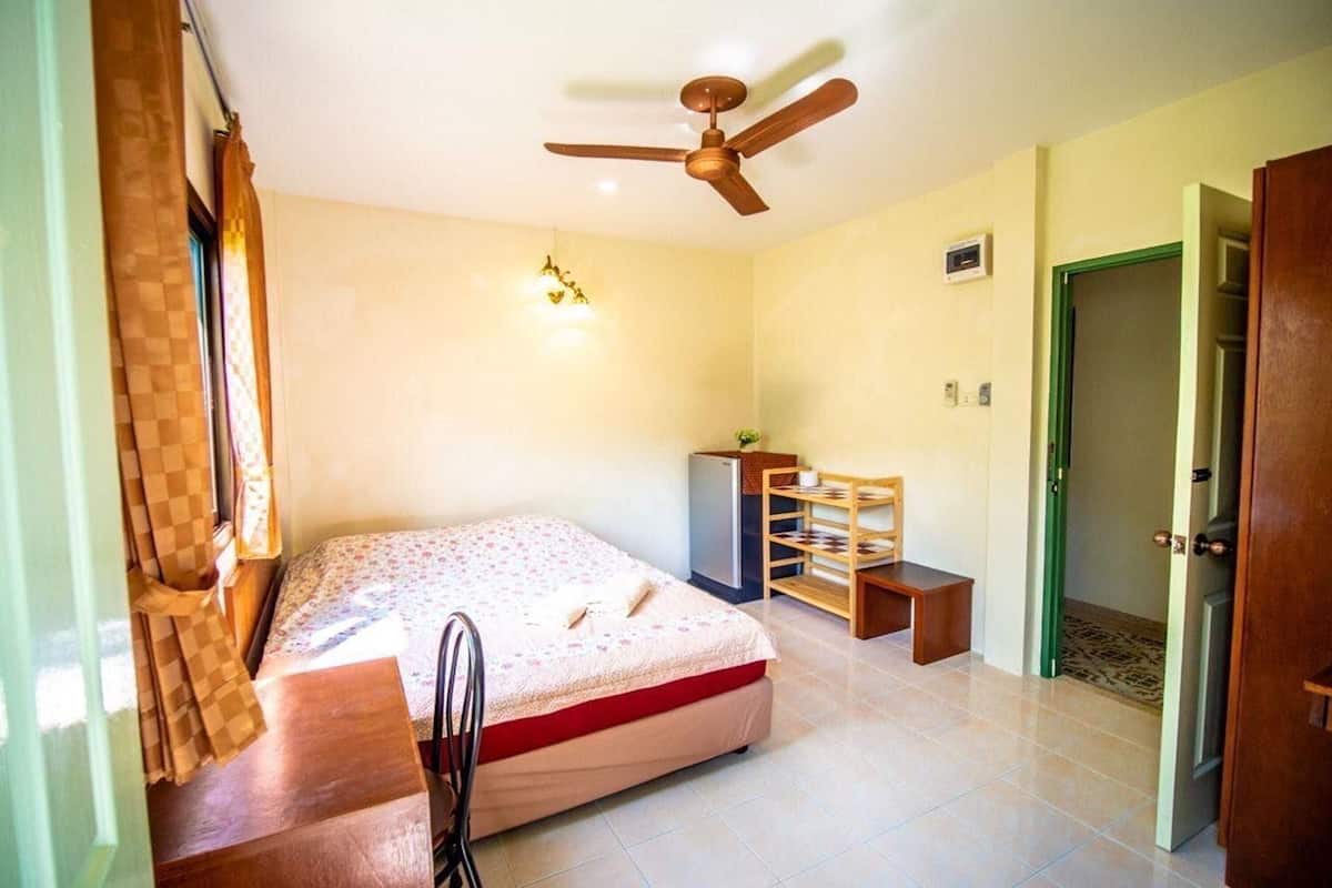 A bedroom with a bed, a ceiling fan, a desk, and a chair.