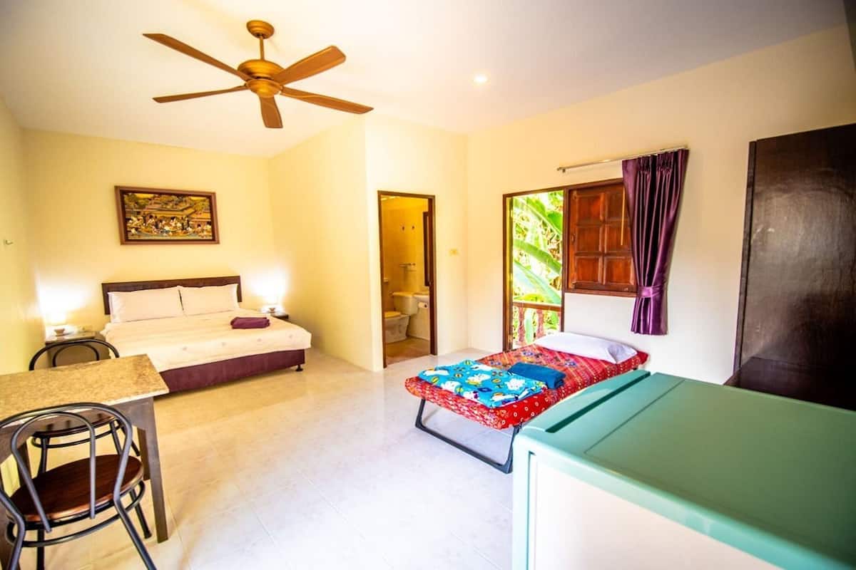 A room with a bed, a desk, a chair, a ceiling fan, and a window with curtains.
