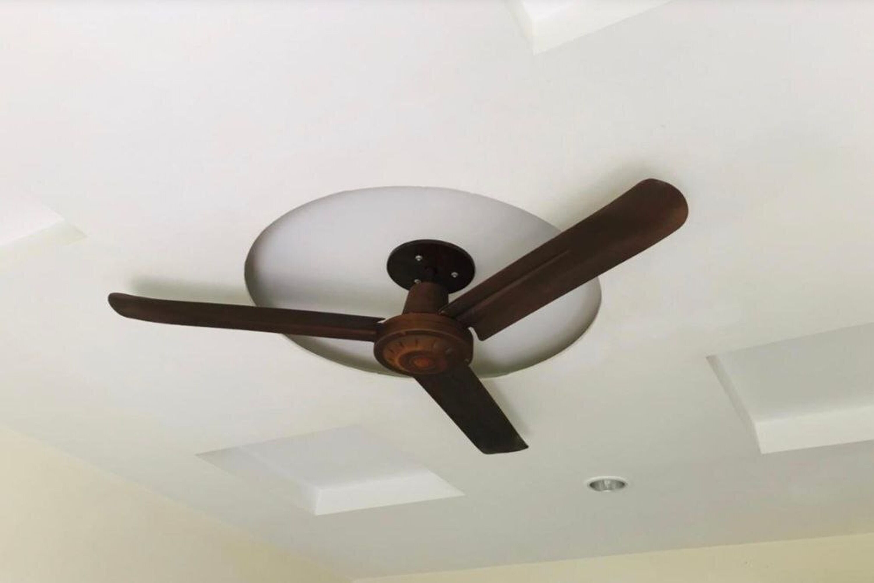 Ein Deckenventilator mit drei Flügeln und einer zentralen Leuchte.