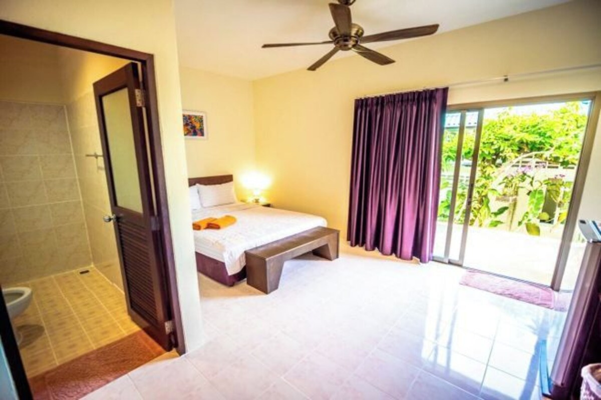 A bedroom with a bed, a ceiling fan, a bathroom with a toilet, and a sliding glass door to a balcony.