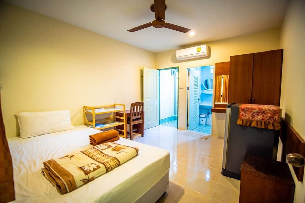 A hotel room with a bed, a desk, a chair, a wardrobe, and an air conditioning unit.