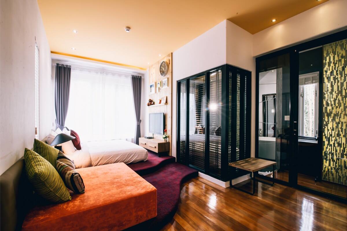 A modern bedroom with a bed, a seating area, a TV, and a wardrobe.