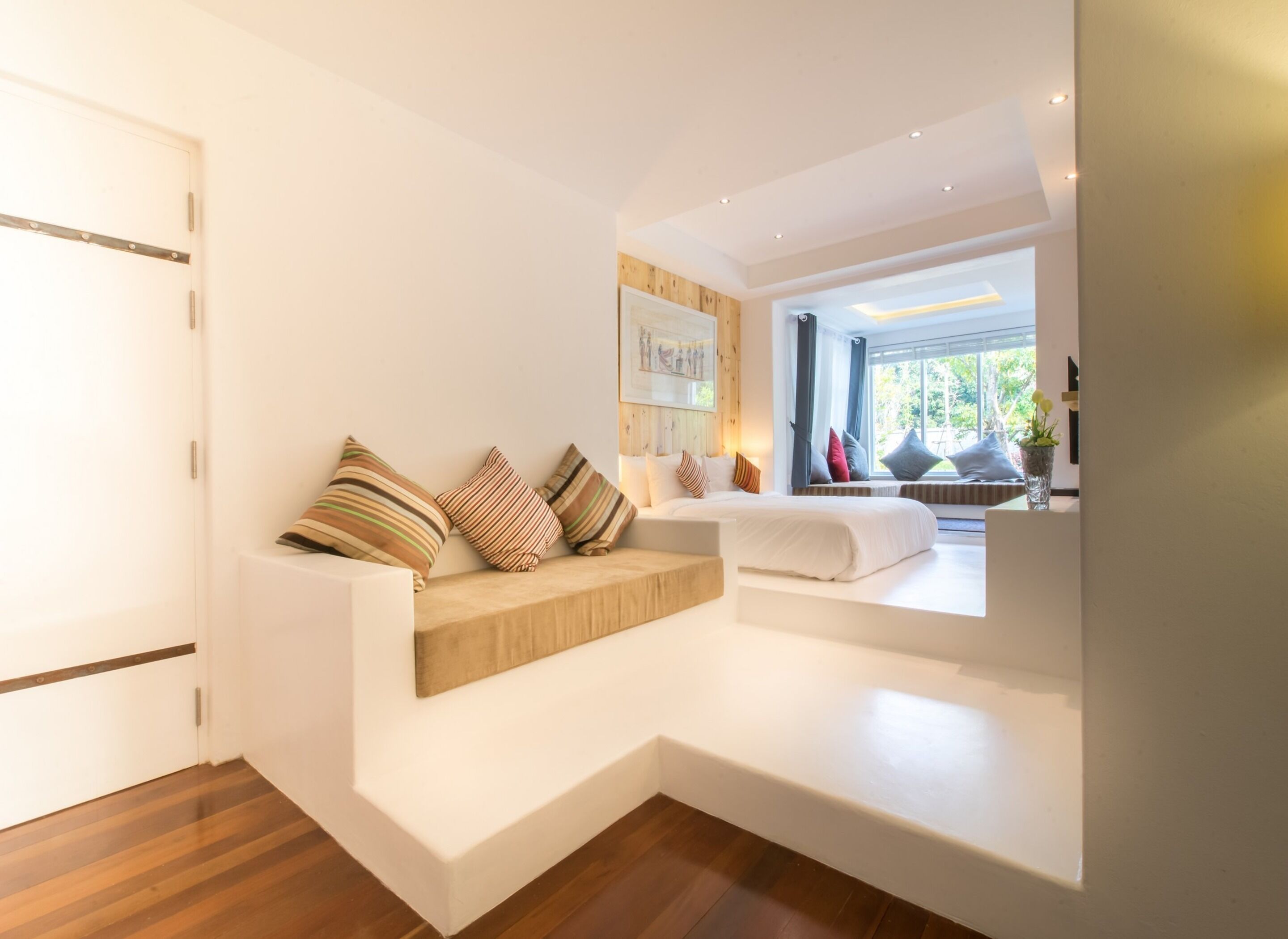 A modern bedroom with a built-in sofa, a large window with a view of greenery, and a wooden floor.