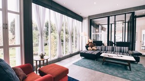 A modern living room with large windows, a sofa, a red armchair, and a coffee table. - Monkey House (Hang Dong)