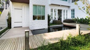 A modern two-story house with large windows, a wooden deck, and a small water feature. - Monkey House (Hang Dong)