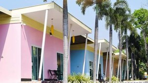 A resort building with a pink and blue facade, palm trees, and a covered outdoor seating area. - AP Grand Resort (Kanchanaburi)