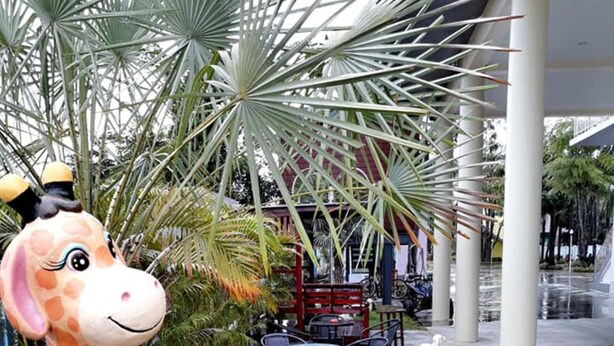 A giraffe statue in a garden area with palm trees and outdoor seating. - AP Grand Resort (Kanchanaburi)