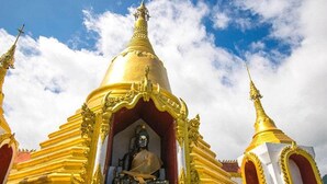 A golden stupa with intricate designs and a seated figure inside, surrounded by golden structures. - AP Grand Resort (Kanchanaburi)