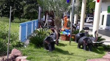 Un jardin aménagé avec des statues d’éléphants en plastique, une clôture bleue et des fleurs jaunes.