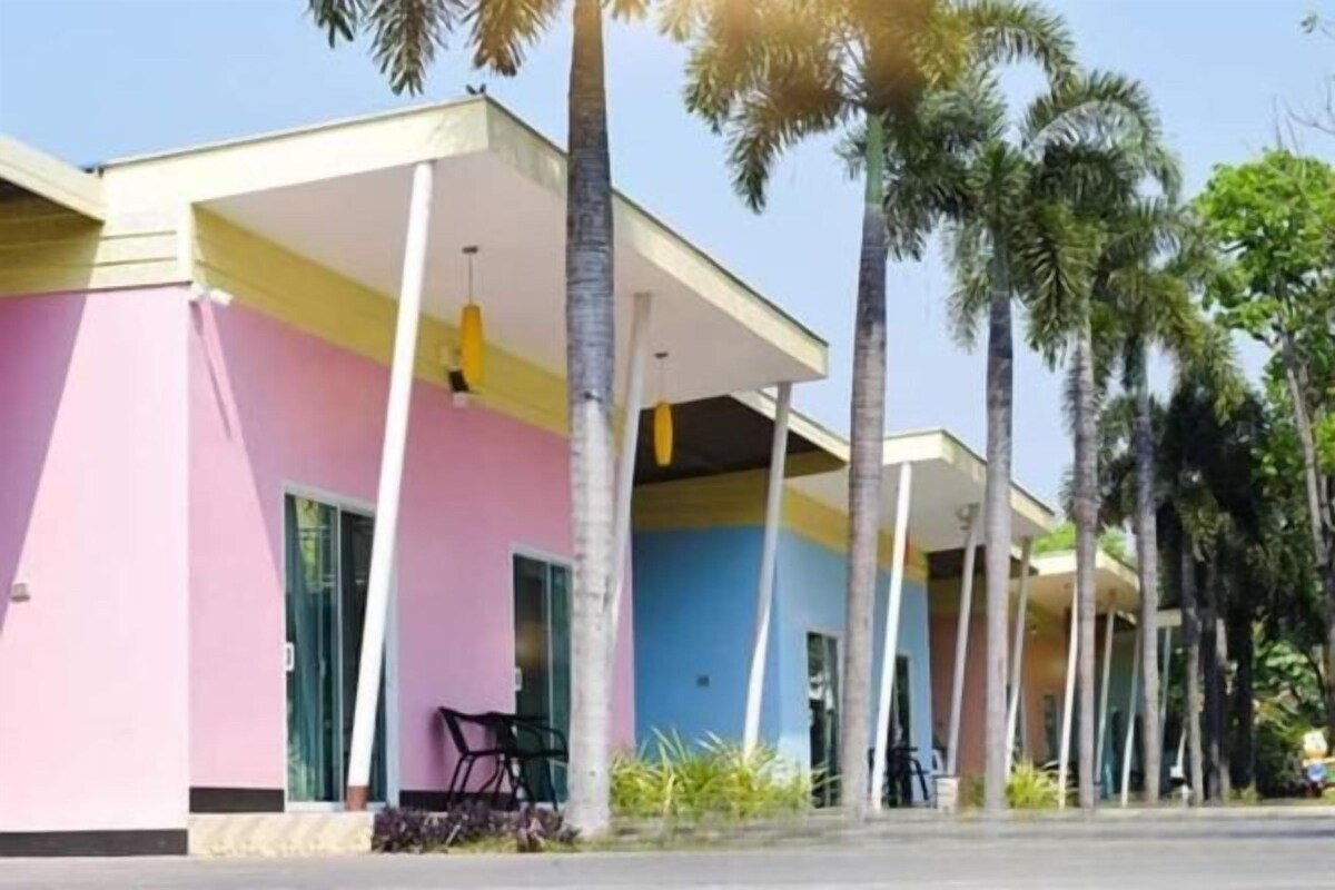 A building with a pink and blue facade, multiple balconies, and palm trees in the background.