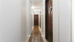 Un pasillo con piso de mármol, paredes blancas y una puerta de madera con un emblema circular.