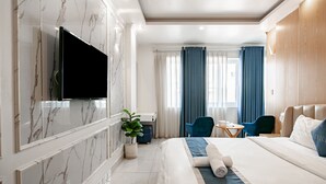 Una habitación de hotel moderna con una cama grande, un televisor de pantalla plana en la pared, un escritorio con una silla y una planta en maceta.