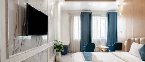 A modern hotel room with a large bed, a flat-screen TV mounted on the wall, a desk with a chair, and a potted plant.
