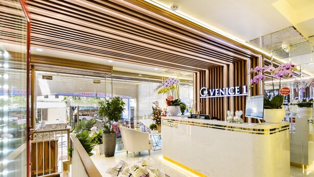 Zona de recepción con un cartel de 'GIVENICE 1', mostrador de recepción, una silla blanca y plantas en macetas.