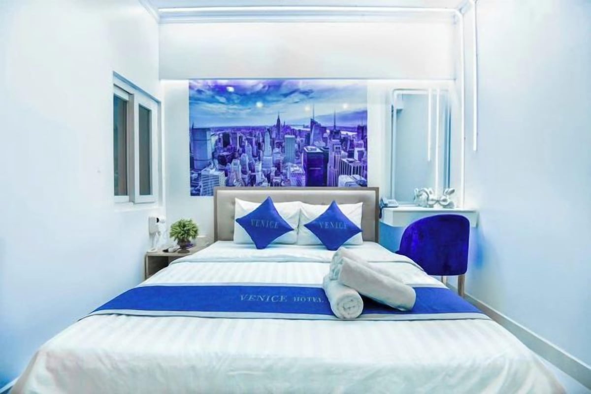 A hotel room with a bed, a nightstand, a mirror, and a cityscape mural on the wall.