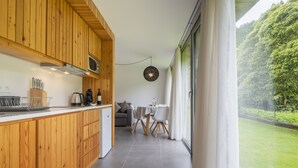 A modern kitchen with wooden cabinets, a dining area with a table and chairs, and a view of a green garden through large windows.