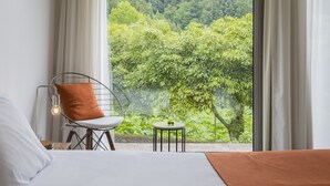 A bedroom with a large window, a bed, a chair, and a small table.