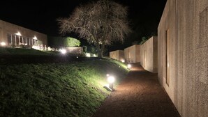 A nighttime pathway flanked by buildings with illuminated windows and a tree in the background.