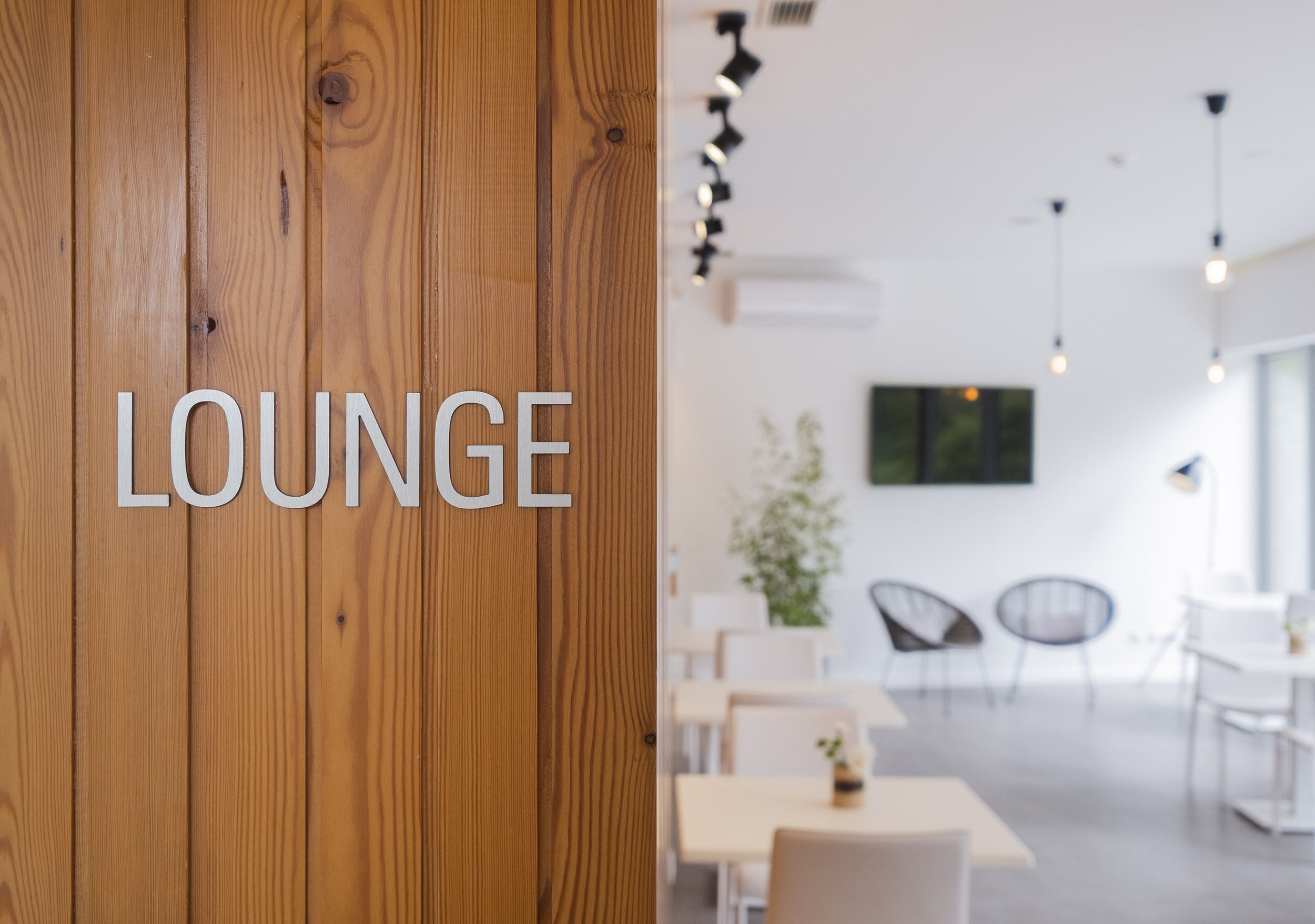 A wooden wall with the word "LOUNGE" and a modern interior with tables and chairs.