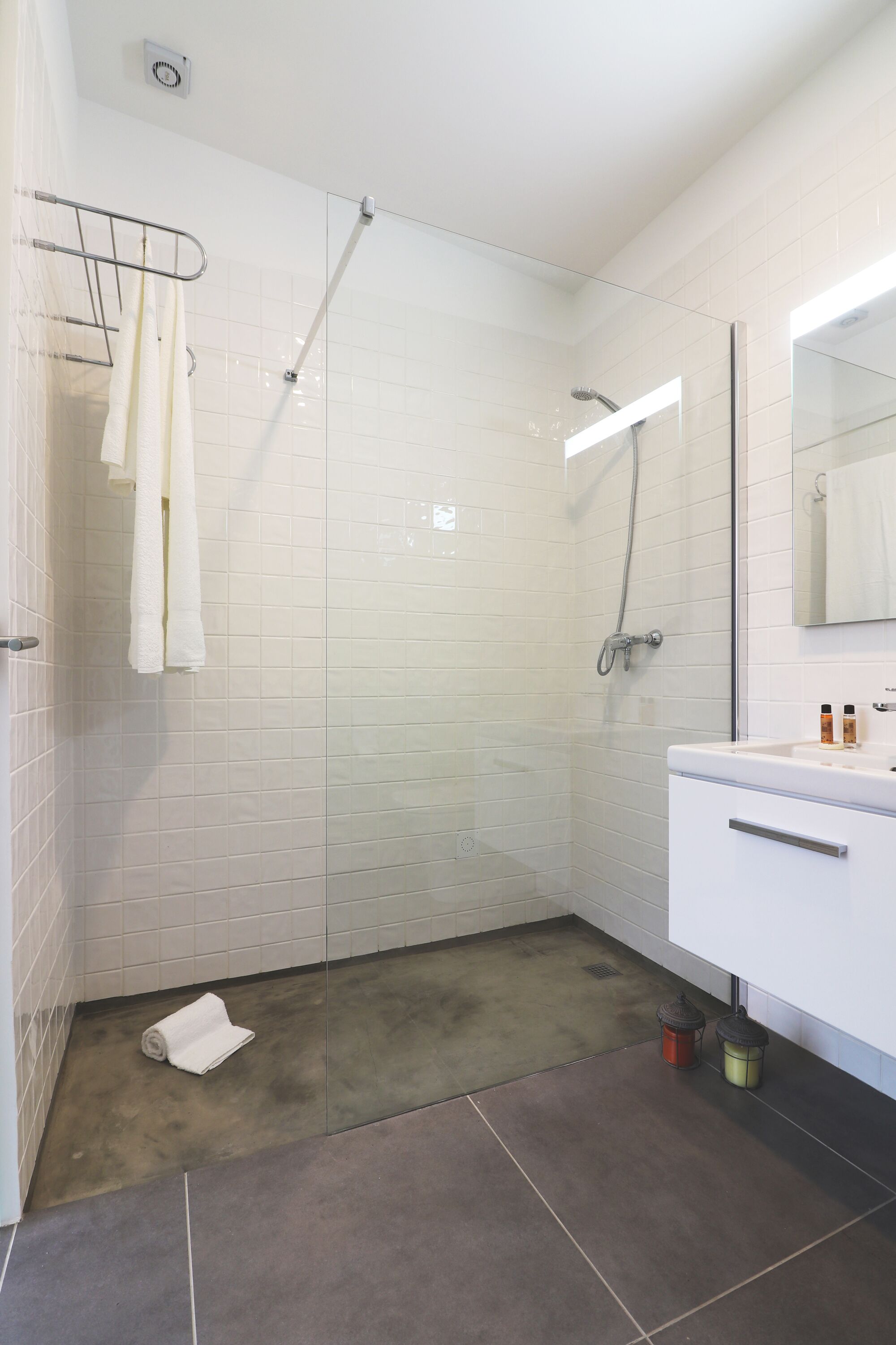 A modern bathroom with a glass shower enclosure, white tiles, and a white vanity with a mirror.