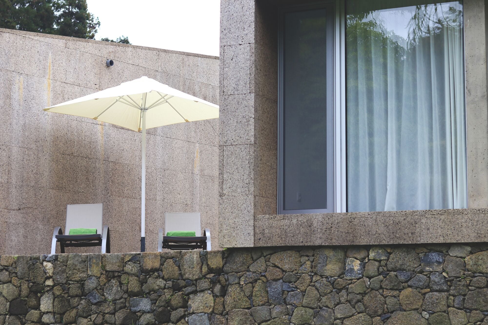 A stone wall with two lounge chairs and a large umbrella.
